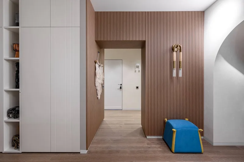 Entryway: floor-to-ceiling wardrobe with open shelves, wooden slat wall and pouf
